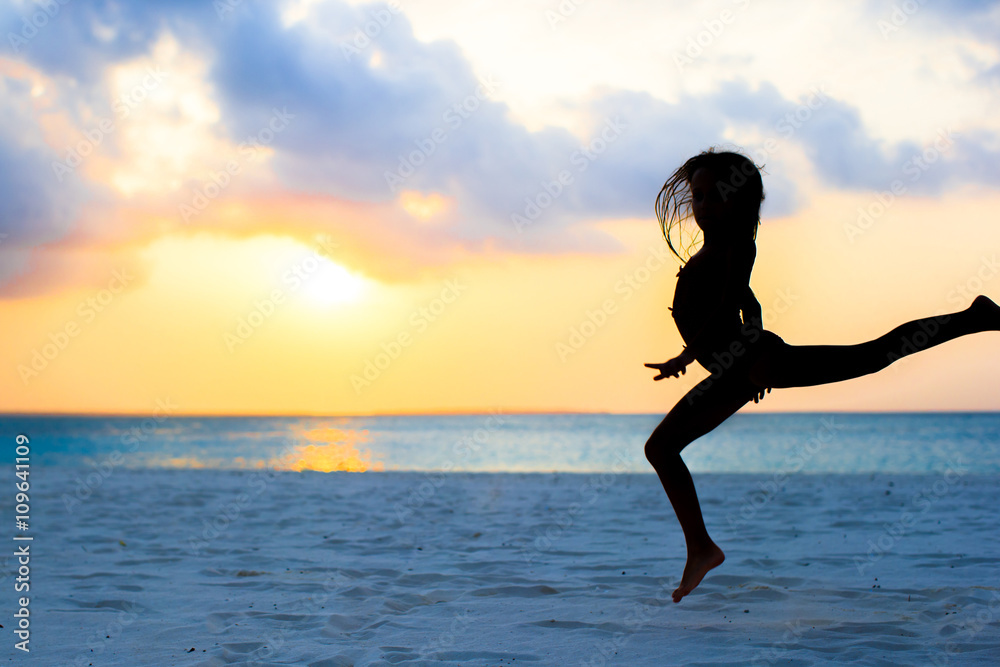 Active little girl jumping on white beach at sunset