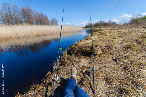 Eye view of fisshing process. Fisherman sitting on the river with two fishing rods. Sunny fishing day on the rever. Mans weekend. photo