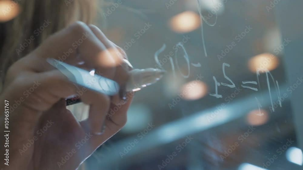 Femanine hands writing on glass whiteboard with white marker, close up