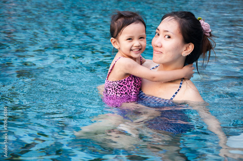 Young pretty girl playing with her mother in pool with clear wat