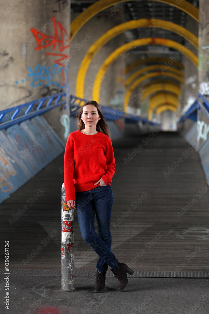 Beautiful Asian woman in red sweater and blue jeans standing on a bridge