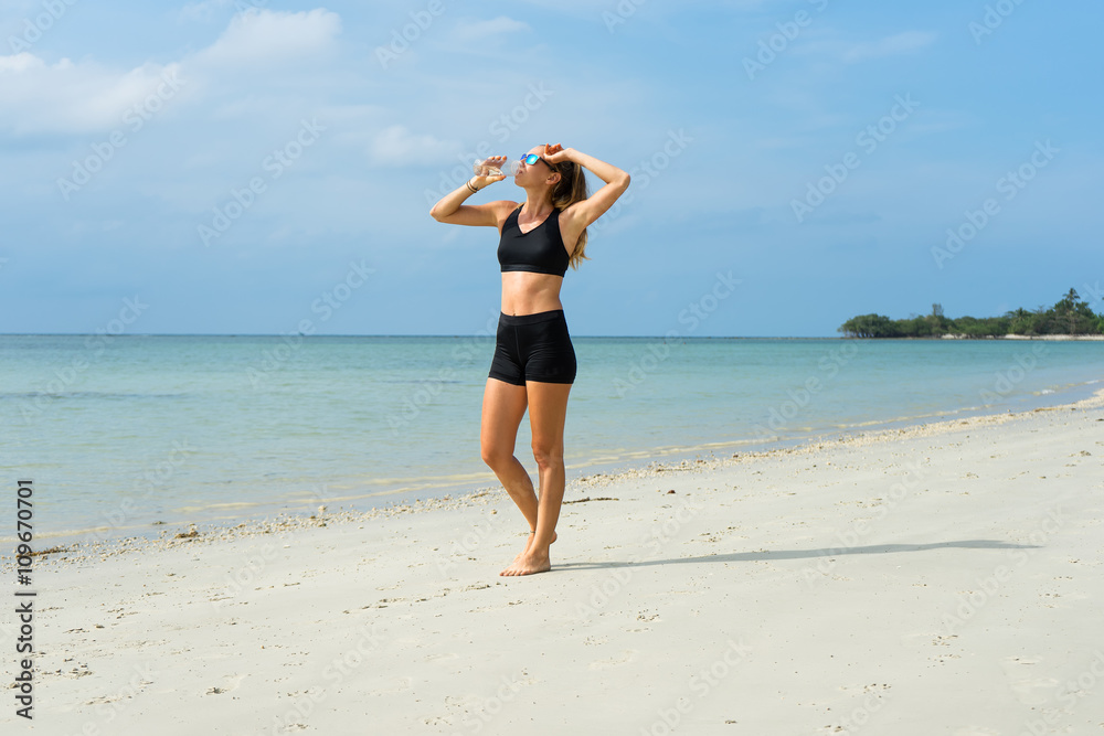The girl on the beach, the sports girl, in hot weather with a water bottle, dressed in black shorts and an undershirt The girl on the beach, the sports girl, in hot weather with a water bottle, dressed in black shorts and an undershirt