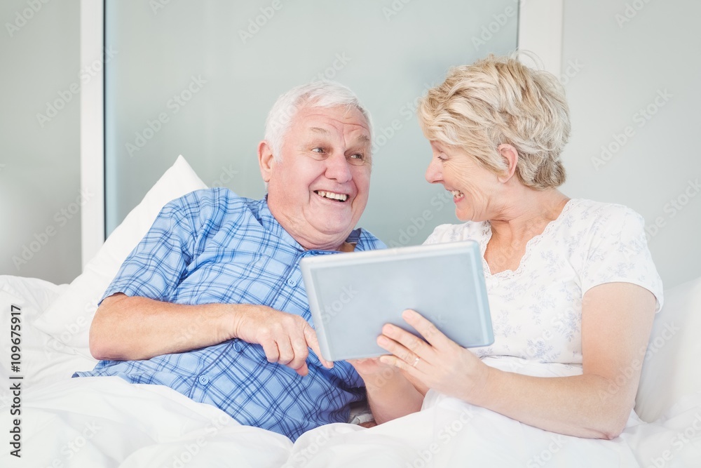 Cheerful senior couple using digital table on bed Cheerful senior couple using digital table on bed