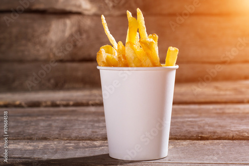 French fries in a cup. Table with cup of fries. Crispy and delicious food. High-fat snack in bistro.