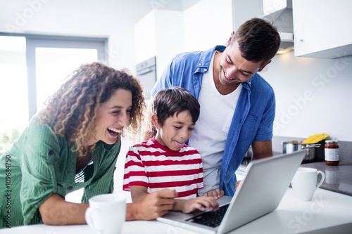 Parents using laptop with son in kitchen