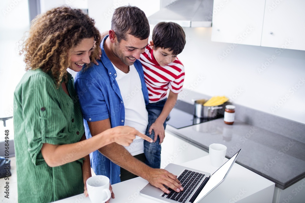 Parents using laptop with son in kitchen Parents using laptop with son in kitchen