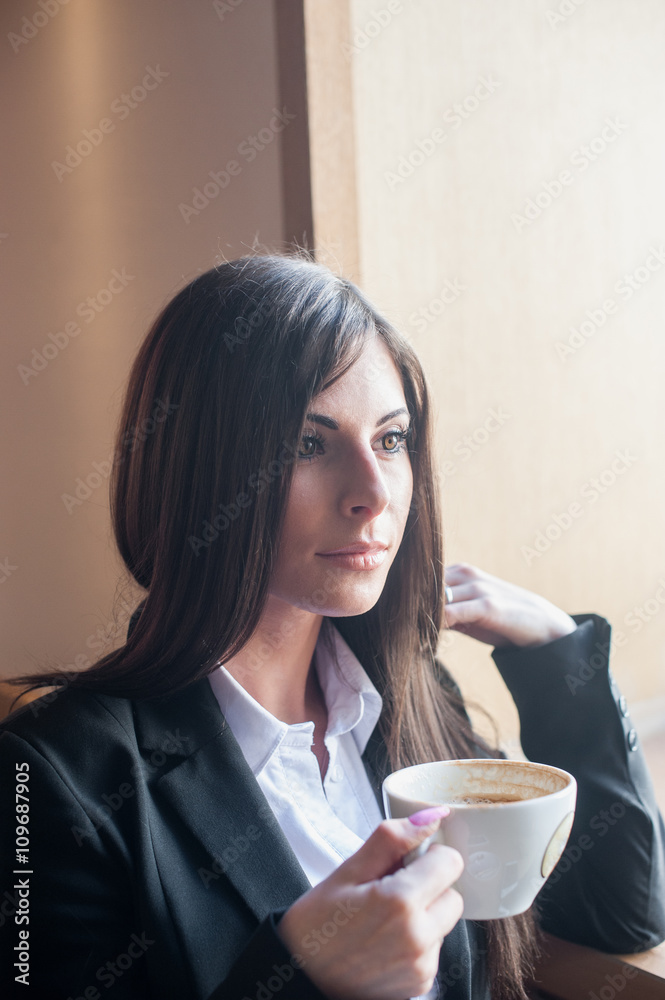 Businesswoman sitting near window and drinking coffee from Cup Businesswoman sitting near window and drinking coffee from Cup