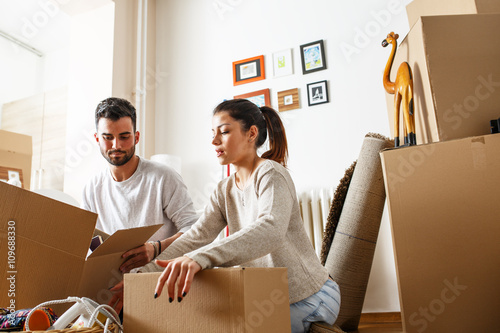 Young married couple moving into new home. They're unpacking card boxes with their accessories.  photo