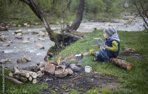 Teenager sitting near a fire in camping and watching map.