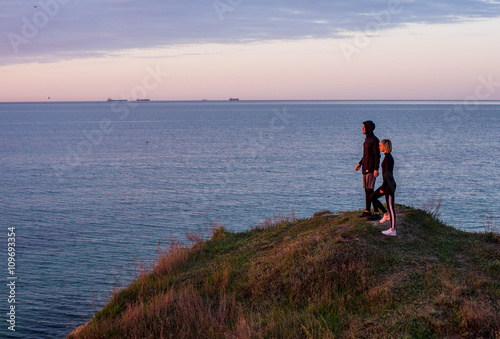 runners man and woman standing on the cliff above the sea during sunset or sunrise 
