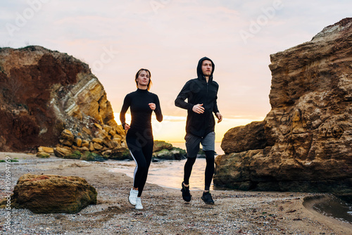 woman and man running on beach. Fit young fitness couple exercising during sunrise or sunset 