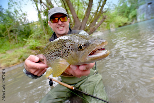 Fly-fisherman holding fario trout caught in river