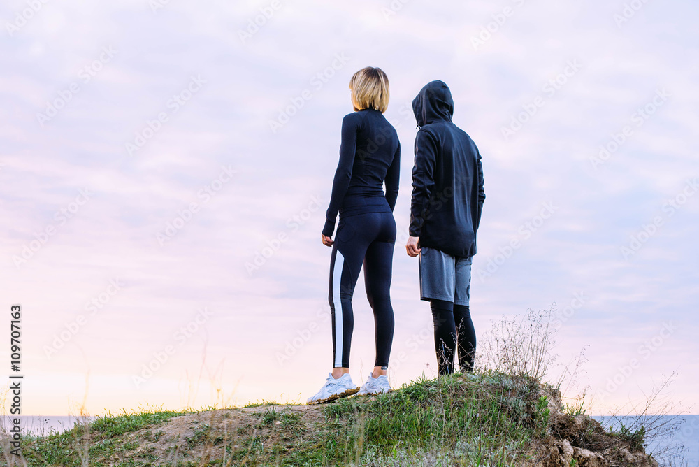 runners man and woman standing on the cliff above the sea during sunset or sunrise runners man and woman standing on the cliff above the sea during sunset or sunrise