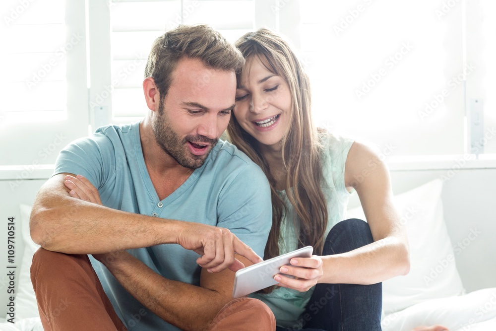 Couple looking in mobile phone while sitting on bed Couple looking in mobile phone while sitting on bed