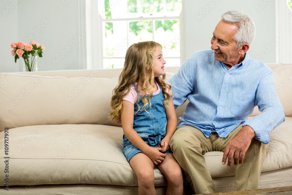 Happy grandfather and girl sitting on sofa 