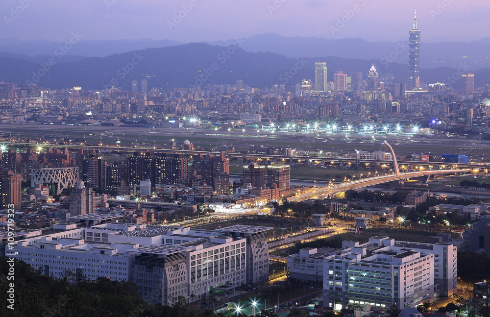Fototapeta premium Panoramiczny widok z lotu ptaka na ruchliwe Tajpej, rzekę Keelung, most Dazhi, lotnisko Songshan i 101 Tower w XinYi District o zmierzchu ~ Romantyczny wieczór w Tajpej z pięknym niebieskim zmierzchem na niebie