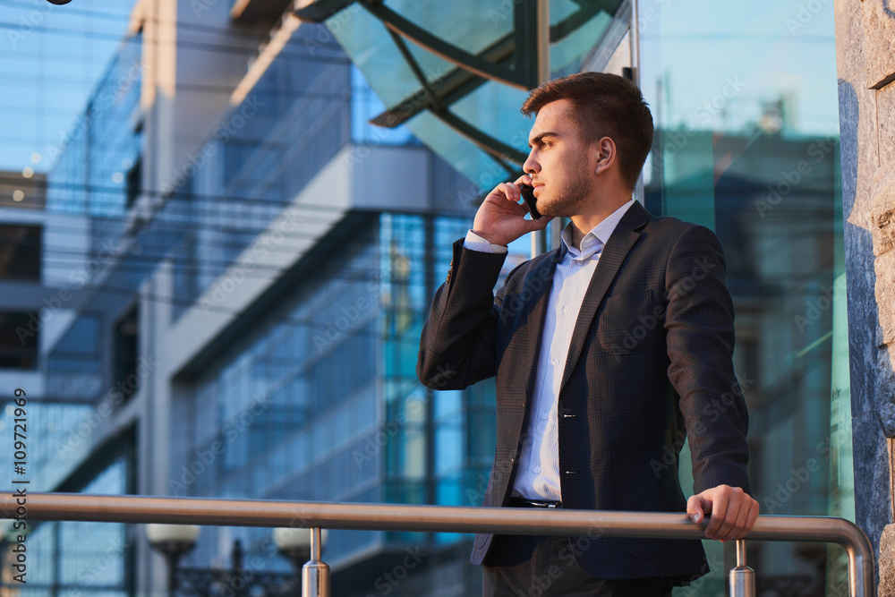Man in suit talking on mobile phone against the building with a glass facade Man in suit talking on mobile phone against the building with a glass facade