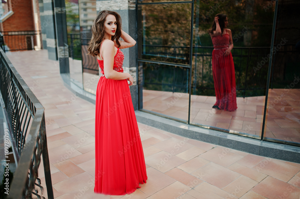 Portrait of fashionable girl at red evening dress posed backgrou