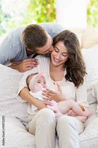 Woman kissing baby while man kissing her from behind