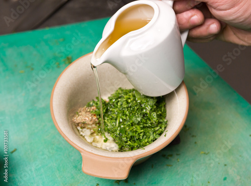 Extra virgin olive oil being poured into a bowl of Organic fresh cut parsley, garlic and herbs.