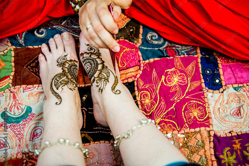Picture of human legs being decorated with henna tattoo, mehendi