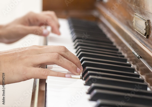 Hands of a skilled musician playing a vintage brown wooden piano by touching the keyboard with talent and gentleness, close up
