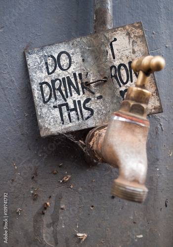 Dirty water tap, with a warning not to drink the water. Water is unsafe for consumption. photo