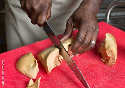 a knife slicing through fresh Foie Gras, on a red cutting board.