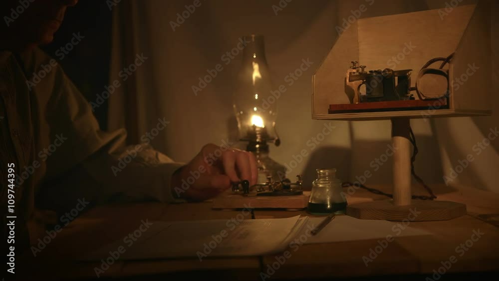 A telegrapher from the old American west era in a in a dimly lit tent sends a telegraph message.
