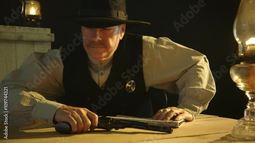 A cowboy from the American wild west era lowers his newspaper to reveal a sheriff badge then gets up and leaves with an annoyed expression. photo