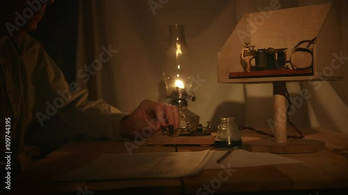 A telegrapher from the old American west era in a in a dimly lit tent sends a telegraph message. photo