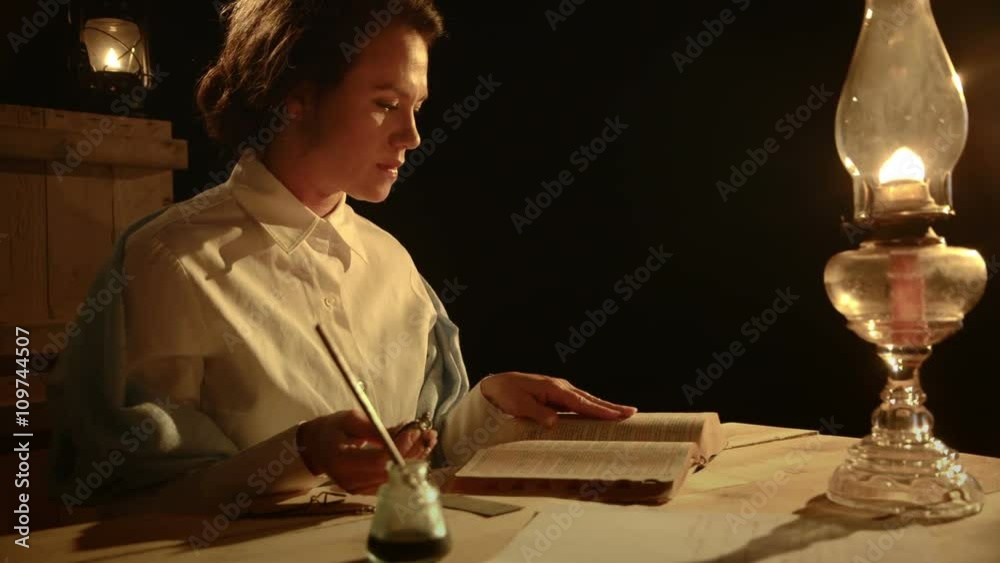 From the early American west era a woman sits and checks the time with a pocket watch then reads from her Bible.