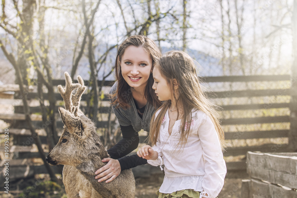 Fototapeta premium Beautiful little girl and her mom hugging animal ROE deer in the