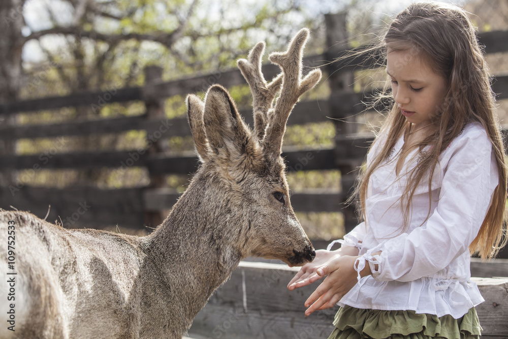 Fototapeta premium Beautiful little girl hugging animal ROE deer in the sunshine