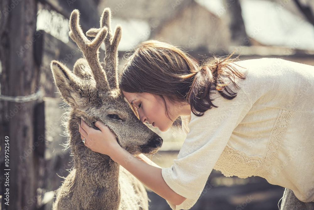 Fototapeta premium Young beautiful woman hugging animal ROE deer in the sunshine