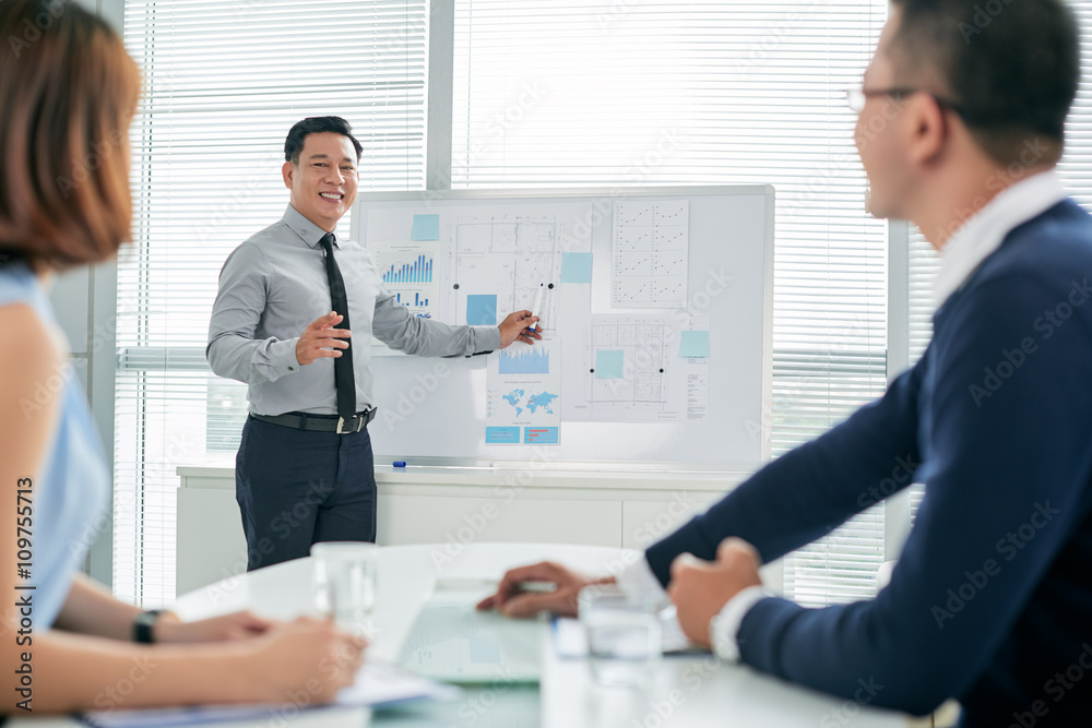 Smiling Asian businessman conducting presentation in front of colleagues Smiling Asian businessman conducting presentation in front of colleagues