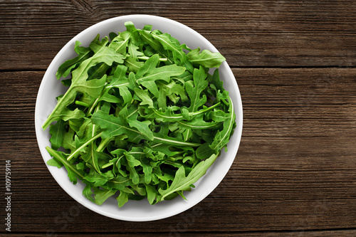 Bowl with fresh green salad arugula on a wooden background