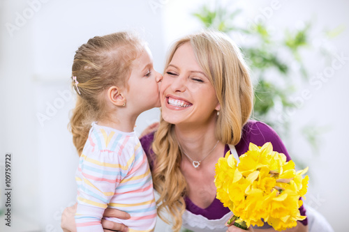 Daughter giving flowers and kiss to smiling happy mohter