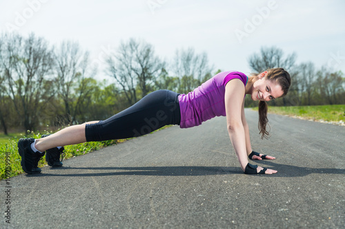 Young woman doing push ups training fitness outside on the road .