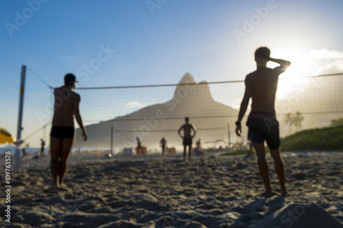Defocused scene of silhouettes of Brazilians playing futevolei (footvolley) against a sunset backdrop of Dois Irmaos Two Brothers Mountain on Ipanema Beach, Rio de Janeiro, Brazil 
