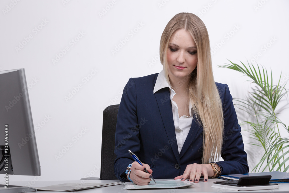 Junge blonde Geschäftsfrau arbeitet am Schreibtisch mit Formularen Junge blonde Geschäftsfrau arbeitet am Schreibtisch mit Formularen