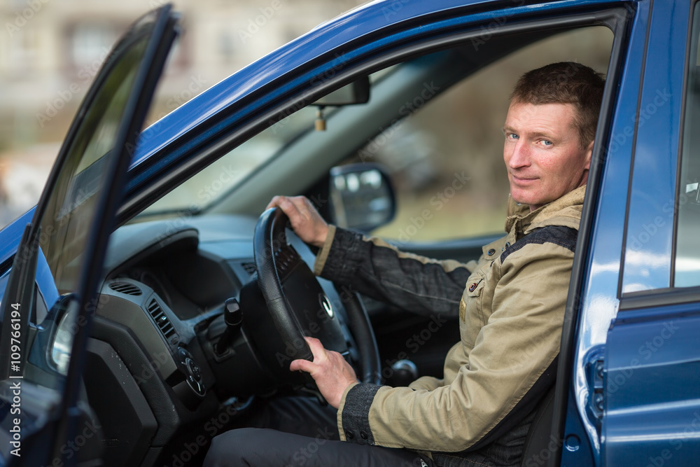 A young man sits in his new car.
