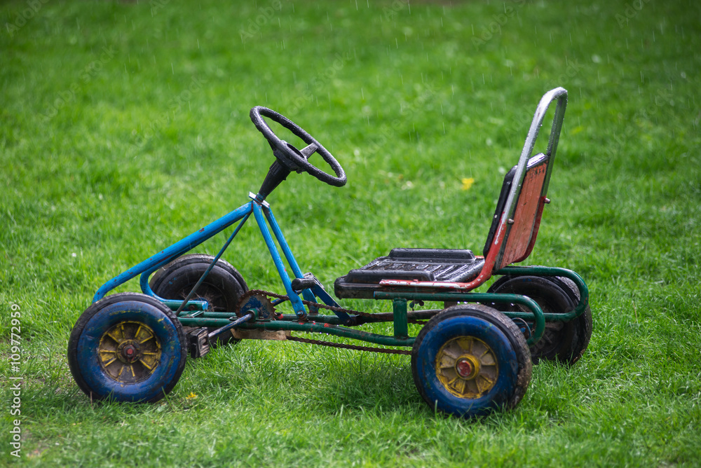 Fototapeta premium Old children's car, standing on green grass in the rain. isolate