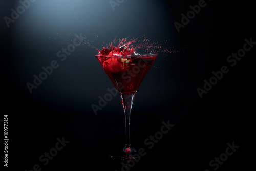 Fresh strawberry falling into a red cocktail in a martini glass photo