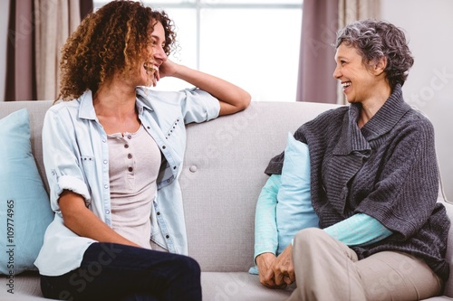 Mother and daughter laughing while sitting on sofa at home