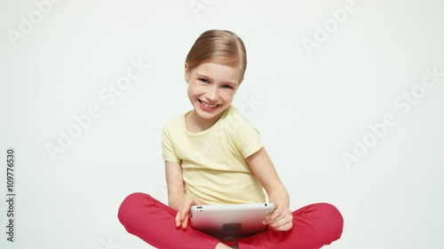 Girl 7-8 years old using tablet pc and sitting on the floor on white background and smiling at camera photo