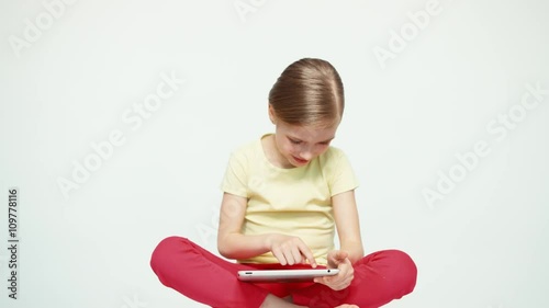 Girl 7-8 years old using tablet pc and sitting on the floor on white background photo