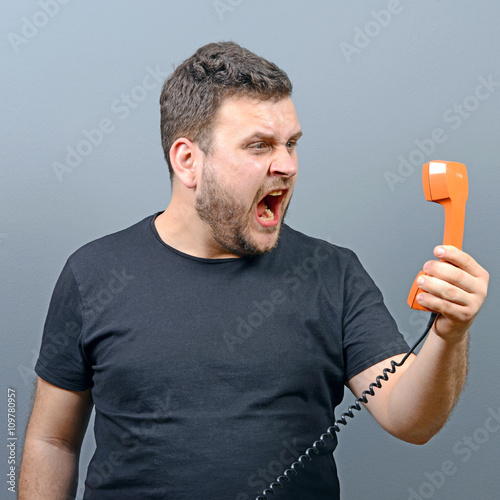 Portrait of funny chubby man shouting on phoner against gray bac