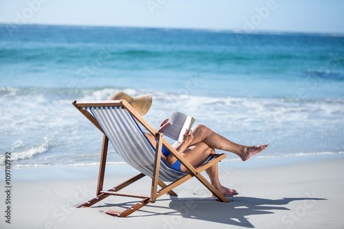 Pretty mature woman reading a book lying on deck chair