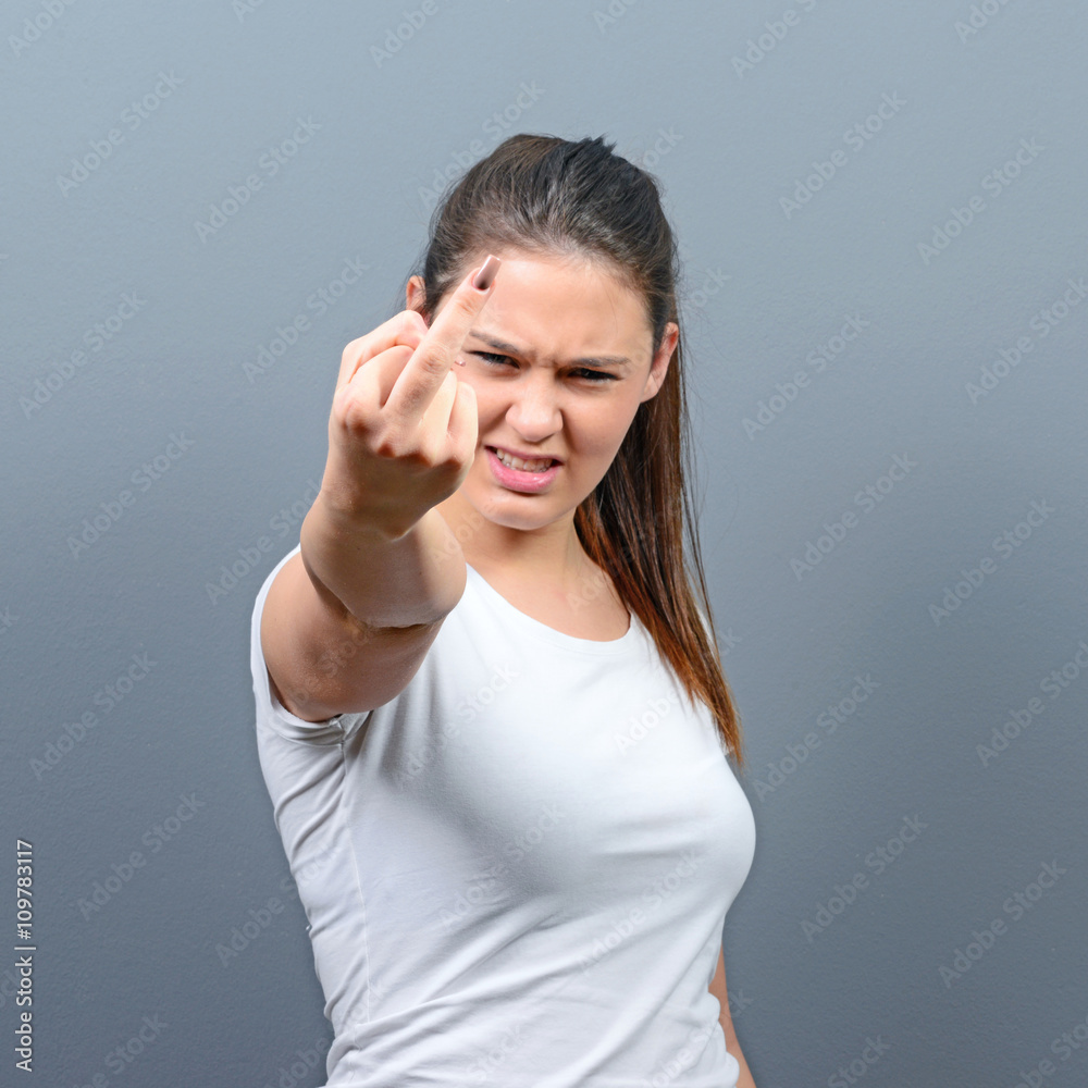 Portrait of a angry woman showing middle fingers against gray ba Portrait of a angry woman showing middle fingers against gray ba